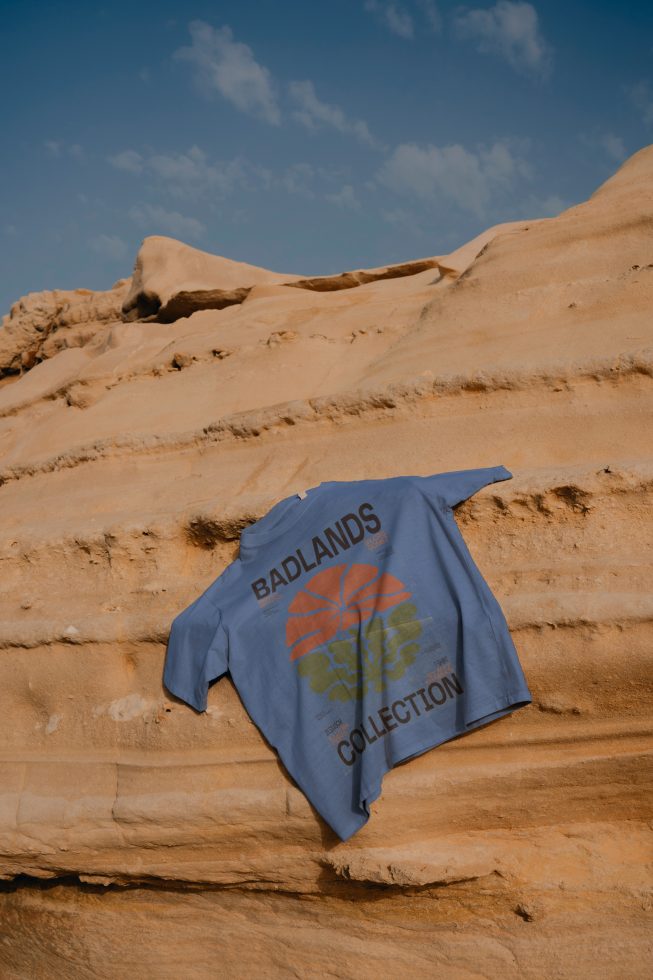 T-shirt mockup with Badlands Collection design laid on desert sandstone, ideal for apparel presentation, outdoor fashion, designer portfolio.