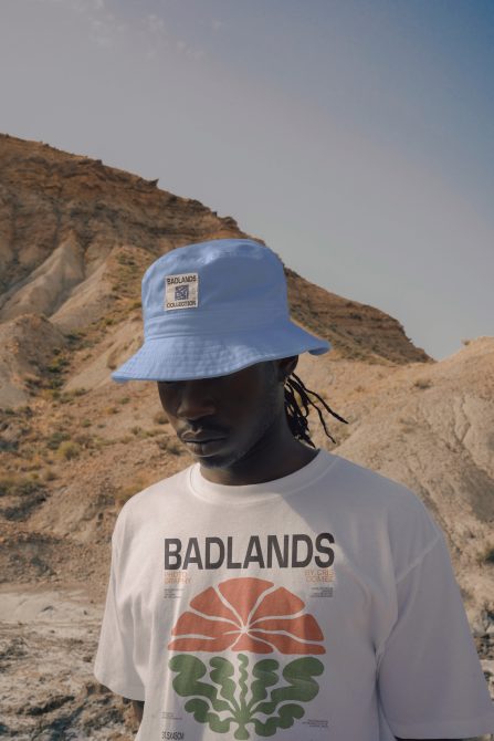 Person wearing white Badlands shirt under blue bucket hat in rocky desert setting