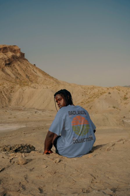 Man sitting in desert wearing blue shirt with Badlands Collection print, perfect for apparel mockups, fashion design.