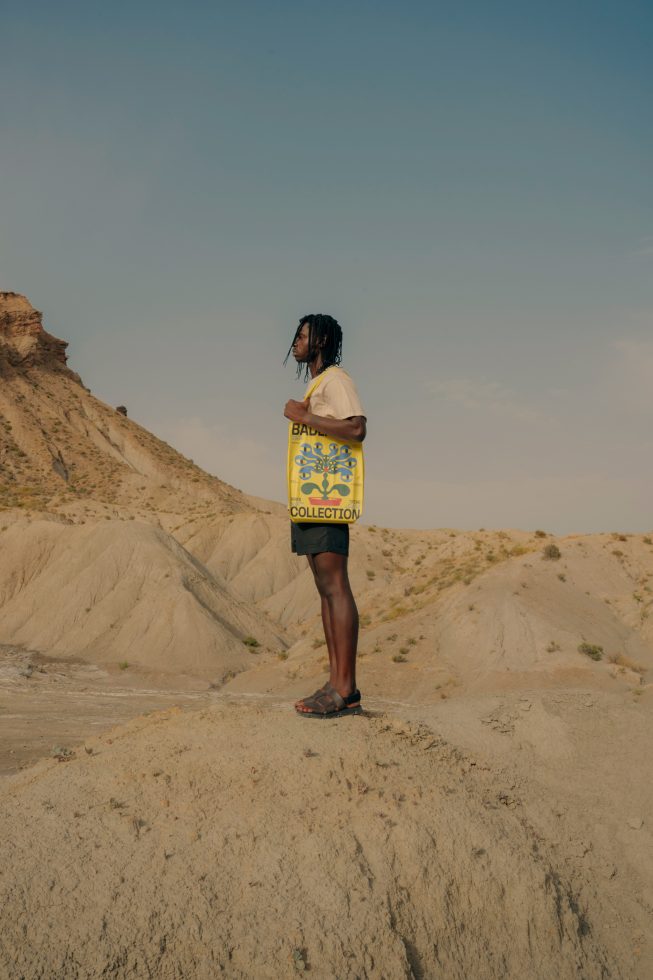 Person in desert landscape carrying bold yellow designer bag for creative fashion mockup or template advertisement, perfect for designers' marketplace.