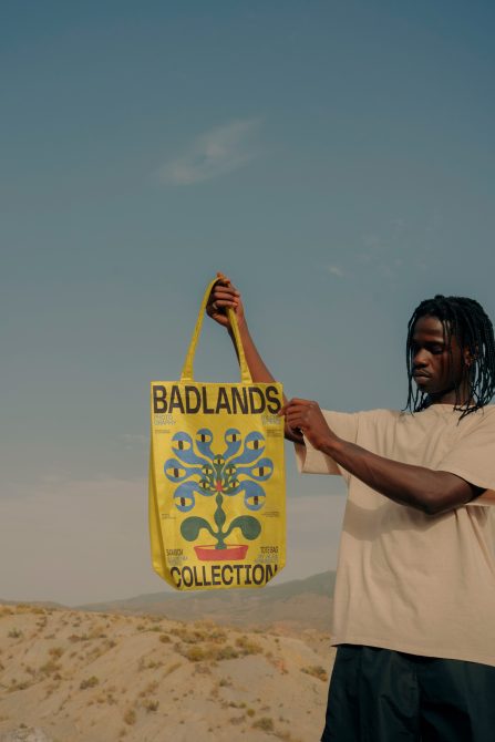 Man holding yellow tote bag with bold graphic design in desert setting, ideal for mockup and print design showcase.