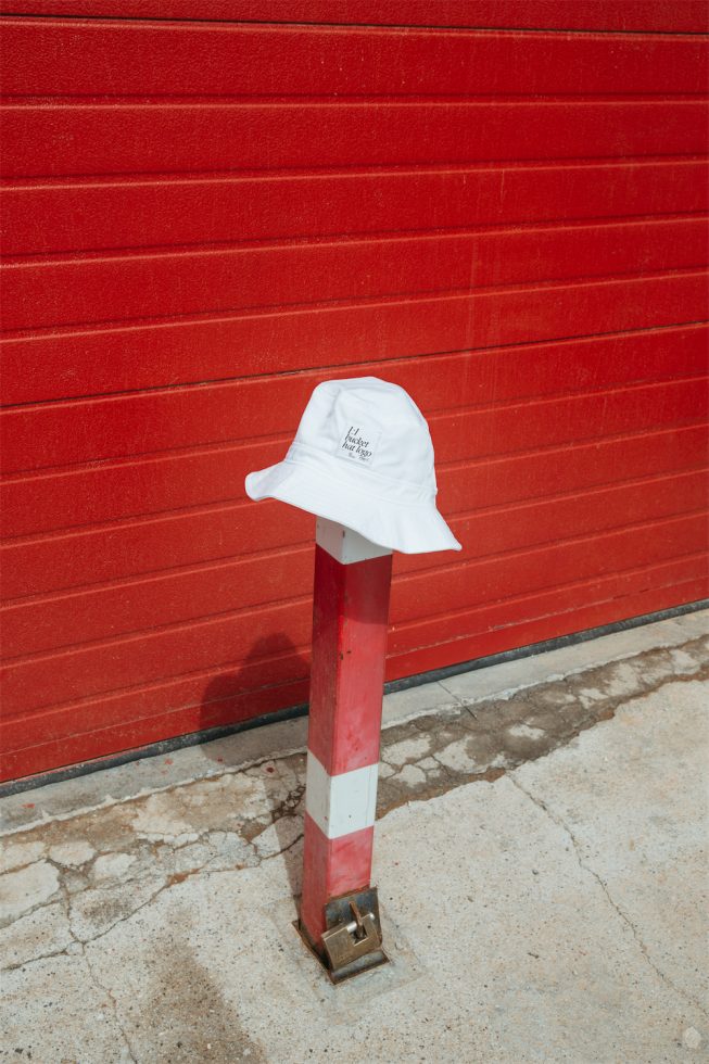 White bucket hat on a bollard with a red textured wall behind, urban fashion mockup, high contrast, clear branding space.