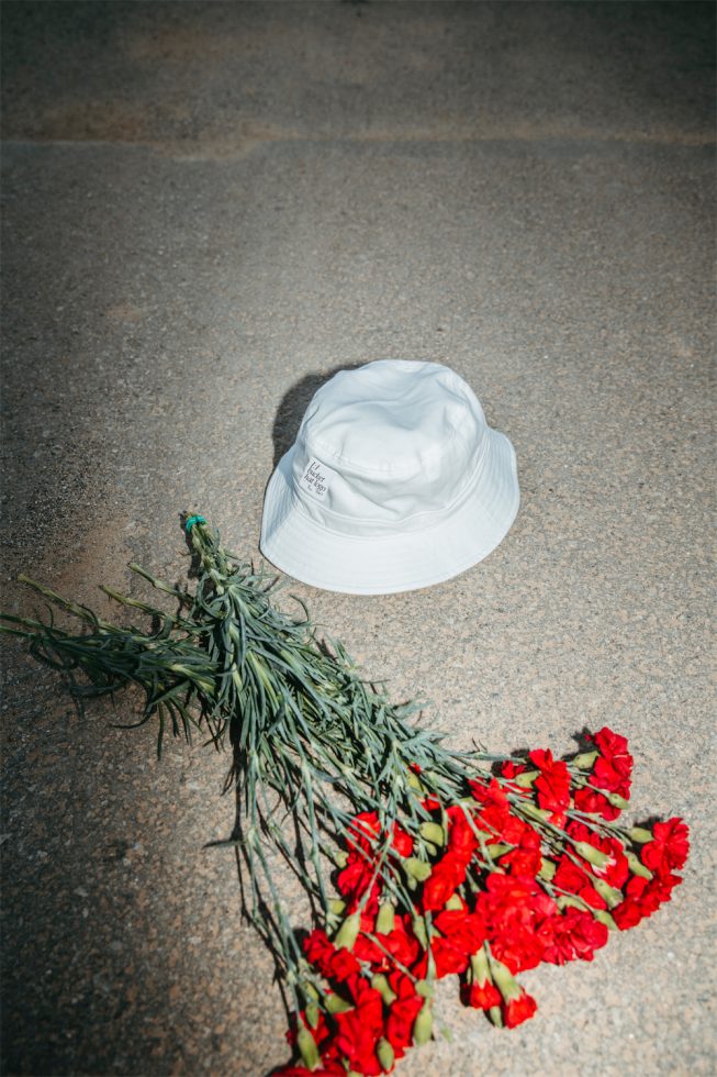 White bucket hat next to red flowers on concrete, streetwear mockup graphic for fashion and apparel designers, urban style template.