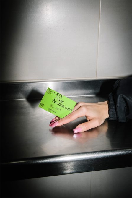 Hand holding a green business card mockup in a stainless steel environment, ideal for presenting design work and branding.