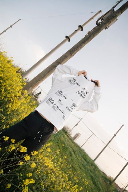Person in white hoodie with text graphics, outdoor setting with yellow flowers, power lines in background, for mockup design assets.