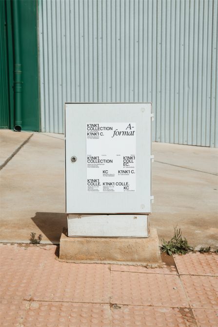 White electrical box with black typographic designs against metal siding, urban street setting, suitable for mockup graphics with editable layers.