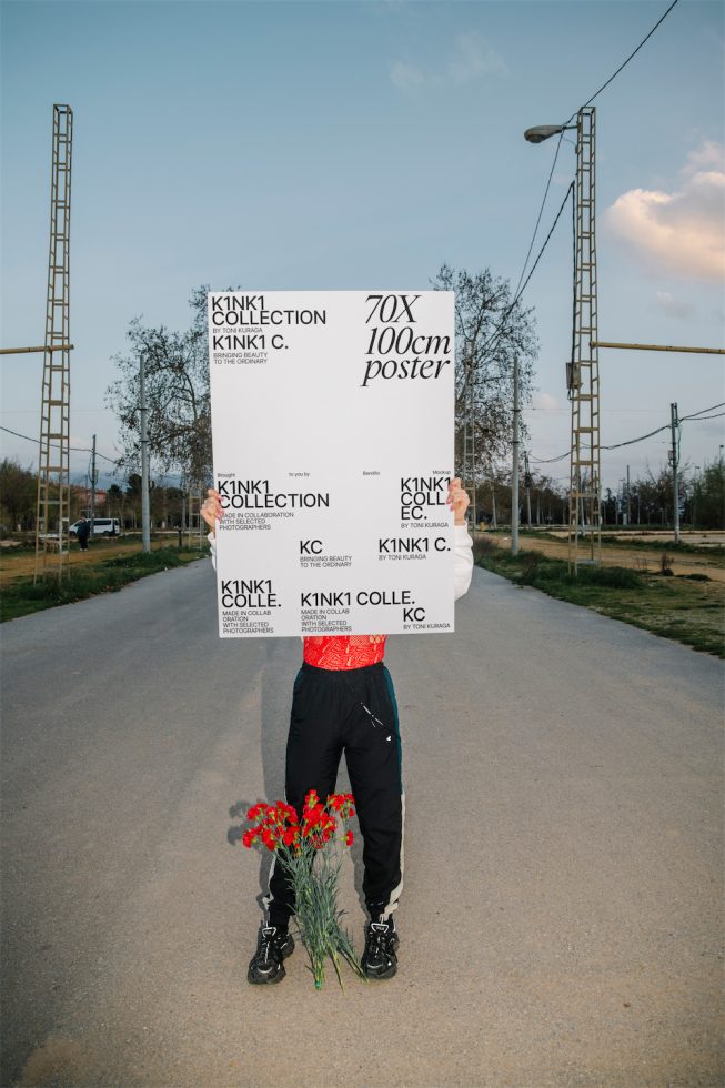 Person holding large blank poster mockup on a street for graphic design and advertising, with clear sky and urban scenery.