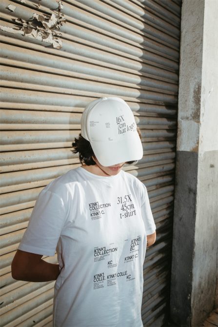 Person in white t-shirt and cap against metal shutter for fashion mockup, urban clothing template, apparel design display with text space.