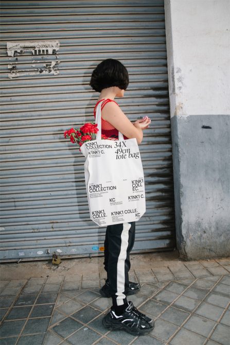 Woman in urban setting with tote bag and red flowers, side view. Ideal for fashion mockups, print design, lifestyle graphics.