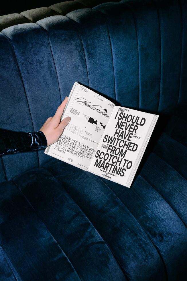 Person holding a magazine mockup with bold typography on blue velvet sofa, perfect for graphic design and font display presentations.