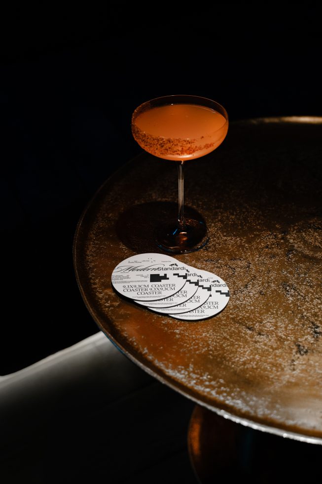 Elegant cocktail on rusty round table with graphic design coaster, perfect for mockup presentations in bar or restaurant branding.