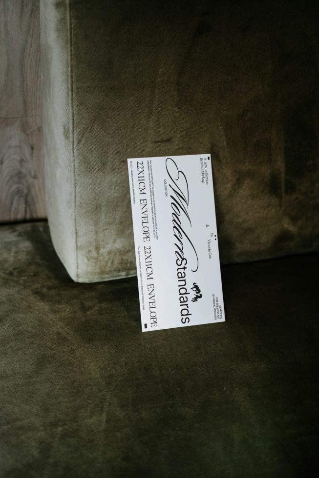 Elegant script font showcased on label for 22x11cm envelope, lying on a textured green sofa, ideal for graphics, stationery mockups, font display.