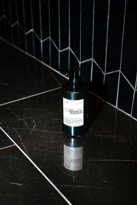 Black dispenser bottle mockup on dark tiled background, ideal for presenting soap or lotion packaging designs for branding.