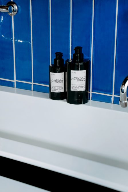 Two black bottle mockups with labels on white sink against blue tile background for product display in bathroom setting, suitable for designers.