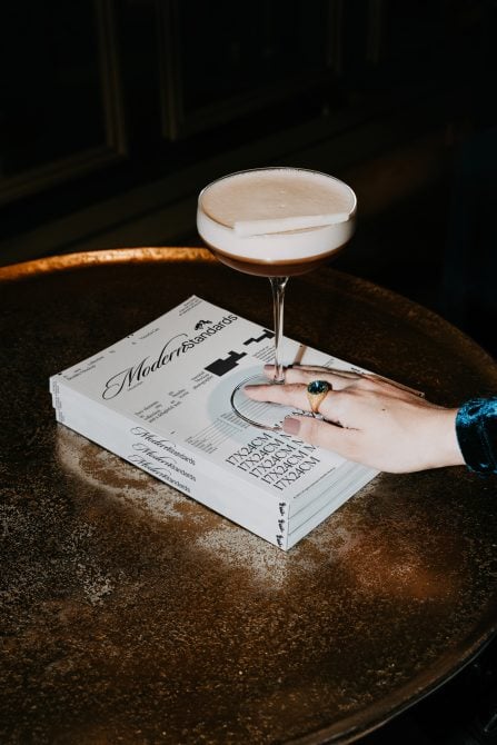 Modern Standards notebook with cocktail, rings, hand on marble table