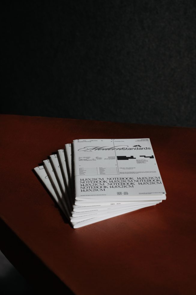 Stack of printed materials with modern typography on wooden table, dark moody lighting, potential mockup or template for designers.