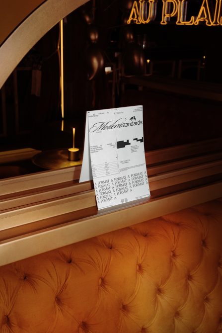 Folded brochure on wooden restaurant bench under gold neon sign Modern Standards design