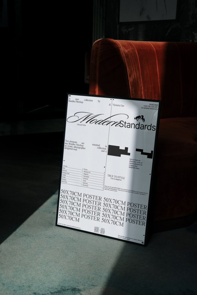 Elegant poster mockup standing on floor beside red velvet sofa, showcasing typography and design layout, perfect for professional presentation.