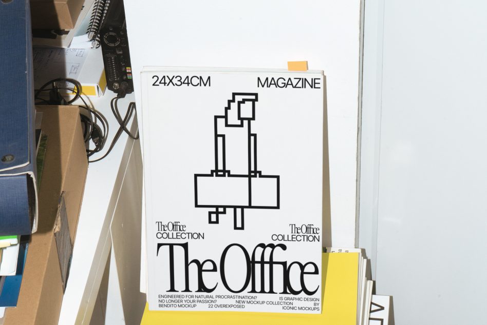 Magazine cover mockup with minimalist office graphic design leaning against white wall, showcasing bold typography and layout.