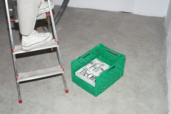 Person standing on a ladder near a green plastic crate with magazines, industrial setting, for mockup graphics and design presentations.