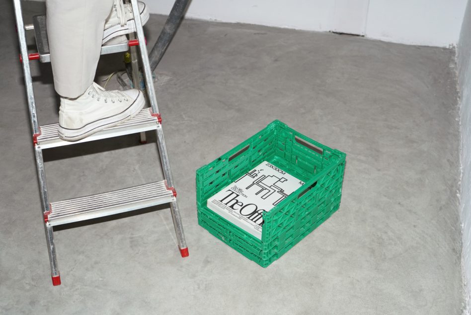 Person standing on a ladder near a green plastic crate with magazines, industrial setting, for mockup graphics and design presentations.