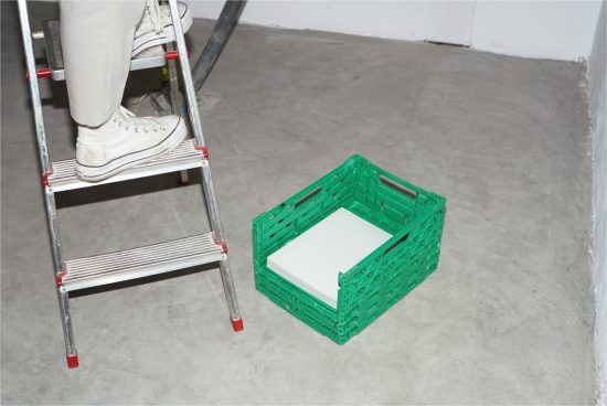 Person on ladder with converse shoes near green crate with white book, minimalist design mockup for presentations.
