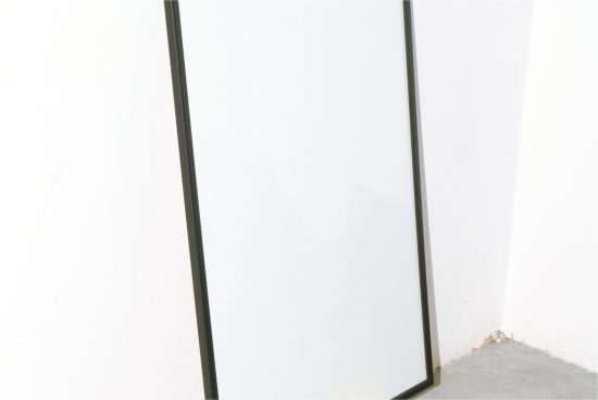 Blank vertical poster frame leaning against a white wall in a bright room, ideal for mockups and graphic design templates.