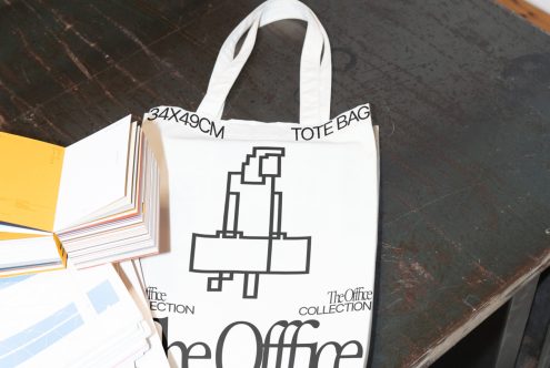 Canvas tote bag mockup with a graphic design, laid on a rustic wooden table alongside assorted colorful paper sheets. Suitable for template display.