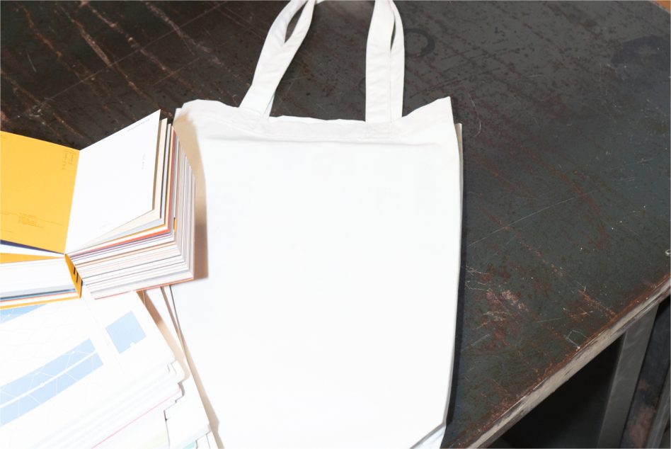 Blank white tote bag mockup on a dark textured surface with colorful paper samples, ideal for branding designs display.