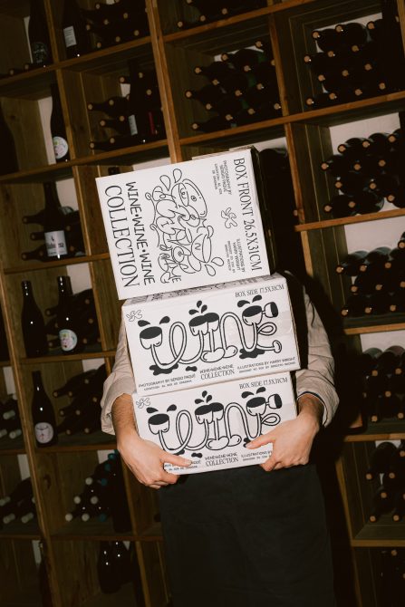 Person holding illustrated wine boxes in a cellar, showcasing bold graphic design packaging, perfect for mockup inspiration for designers.