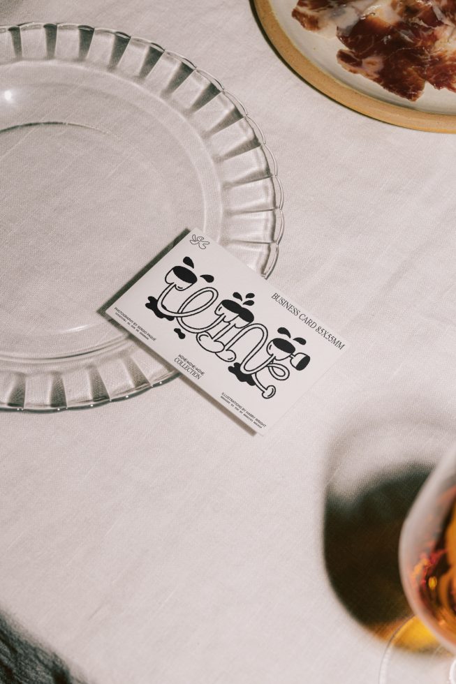 Creative business card mockup on a linen tablecloth with a clear glass plate and food, showcasing playful font and graphics design.