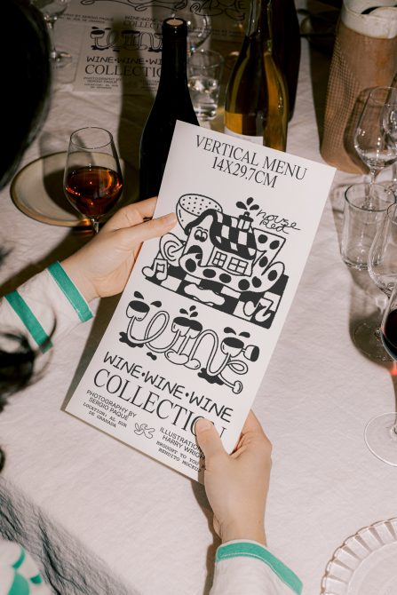 Hand holding a custom wine menu mockup on a table with glasses and bottles, ideal graphic for restaurant branding and template design.