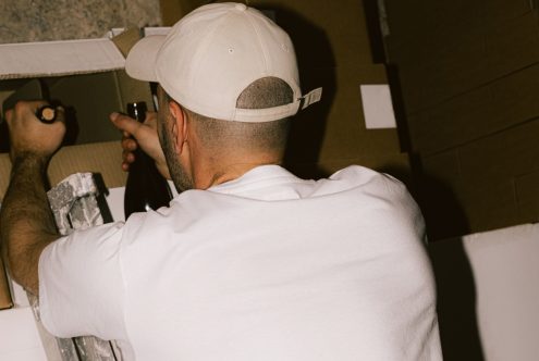 Man in white t-shirt and cap viewed from behind working on project with tools and cardboard, ideal for mockup graphics.