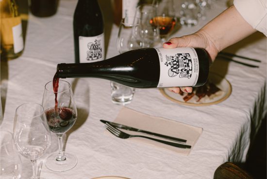 Person pouring red wine into a glass, elegant label design, dining setting, suitable for mockups and graphic templates.