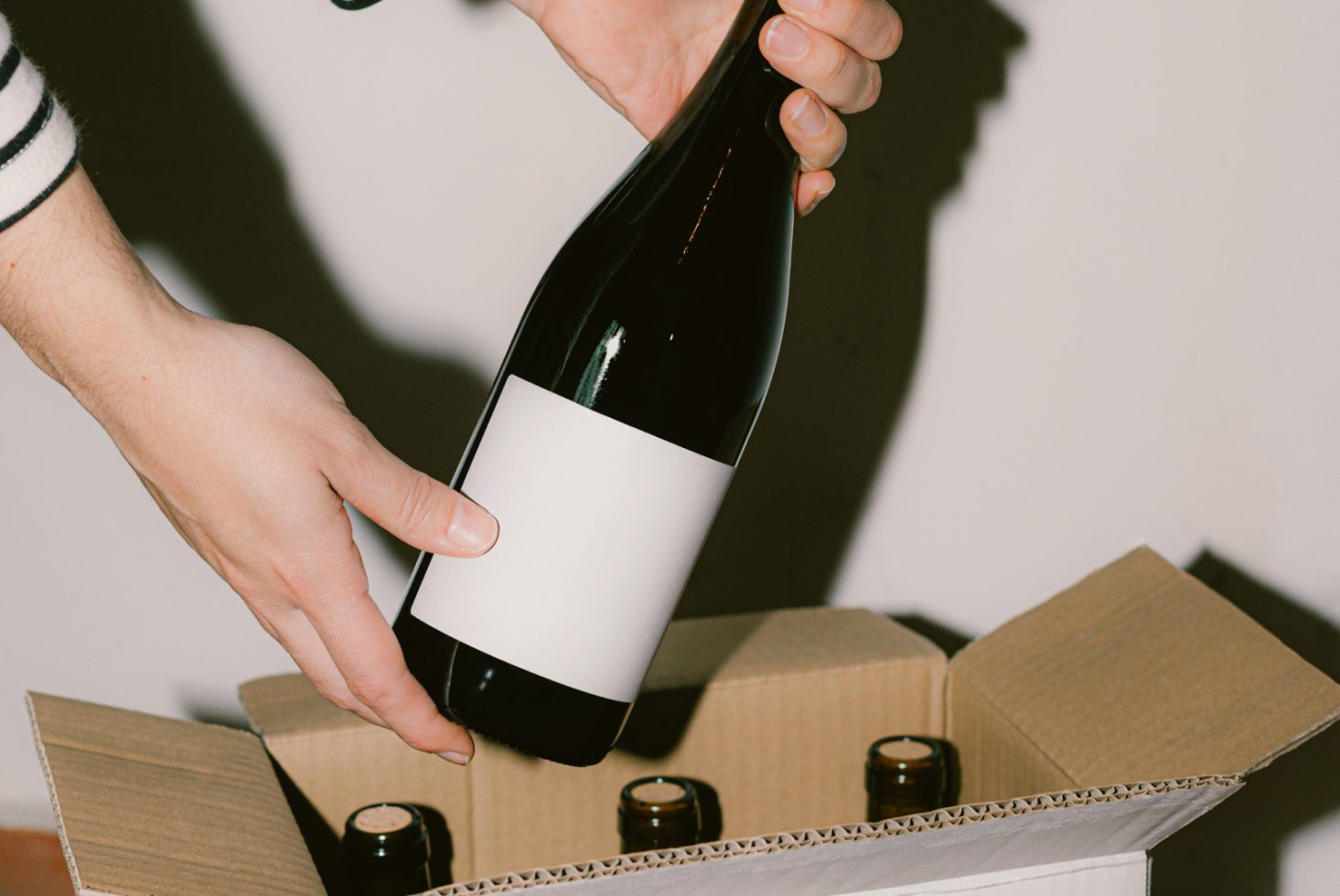 Person holding wine bottle with blank label from cardboard box, ideal for mockup, labels, packaging design, product presentation.