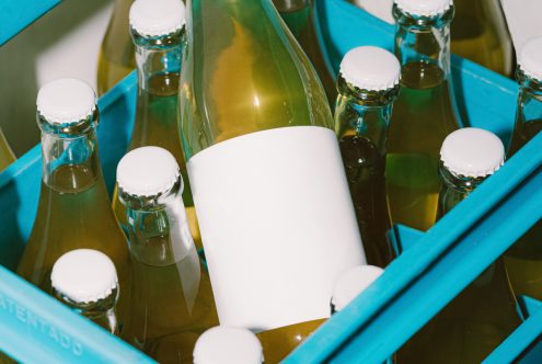 Glass bottles in blue crate with blank label for branding mockup, packaging design, product presentation.