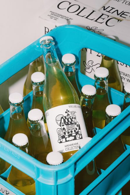 Bottle mockup in blue crate with playful label design, showcasing packaging and label graphics for wine or beverage branding.