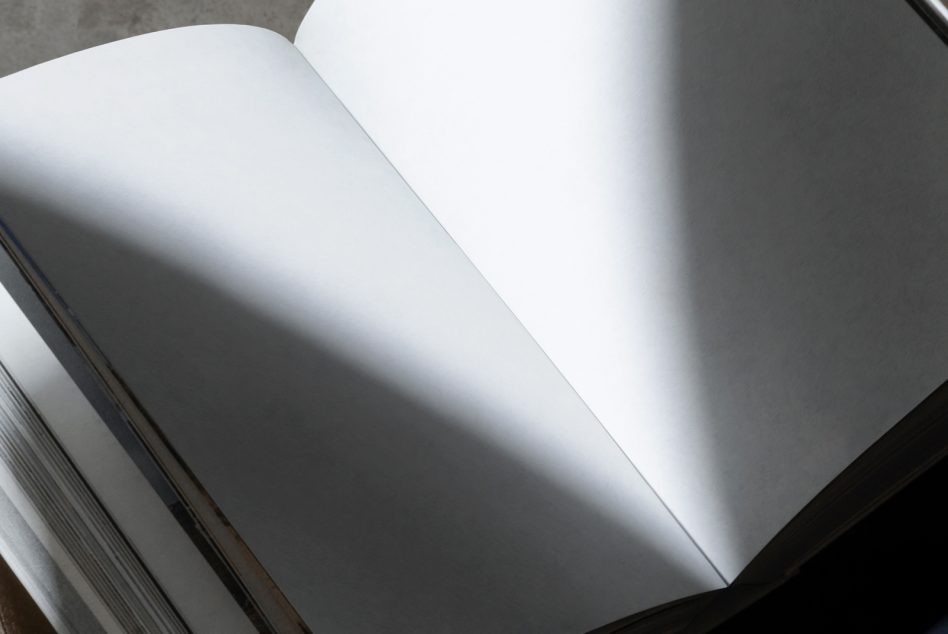 Open spread of blank white pages in book with natural light casting shadow