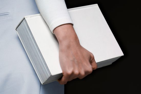 ALT: Close-up of a person's hand holding a blank book mockup for design presentation, isolated on a neutral background, visible texture and detail.