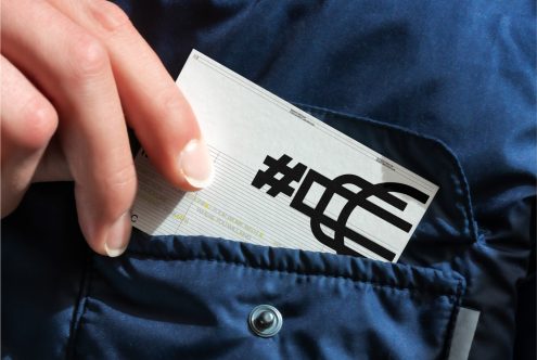 Person holding business card mockup with bold typography design on a dark blue jacket, ideal for branding and stationery presentations.