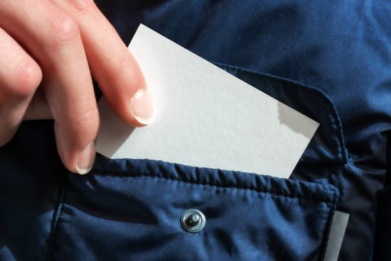Close-up of a hand pulling a blank business card from a dark blue jacket pocket, ideal for mockup design presentations.