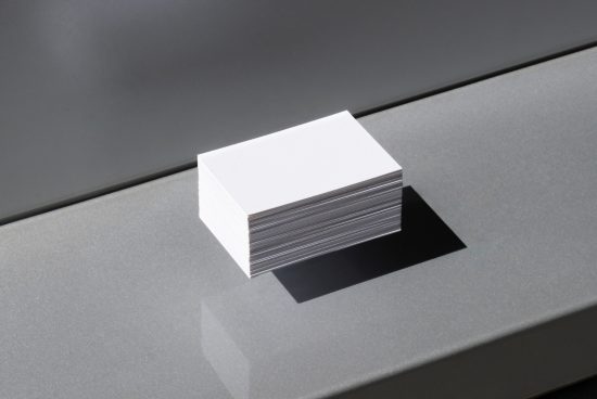 Stack of blank business cards in natural lighting on a textured gray surface, ideal for mockup graphics and templates design.