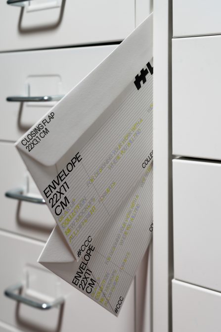 Envelope mockup 22x31cm tucked into white cabinet drawer, neon yellow details visible