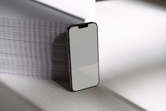 Modern smartphone mockup with blank screen, standing on white surface with shadow pattern for design presentation.