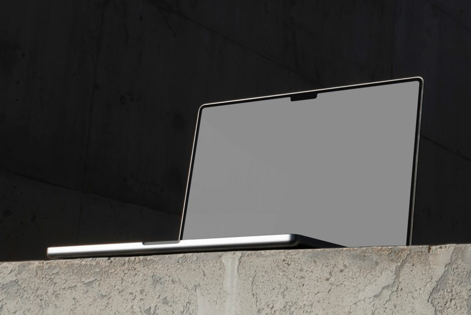 Blank MacBook Pro screen mockup positioned on textured concrete wall in minimal setting