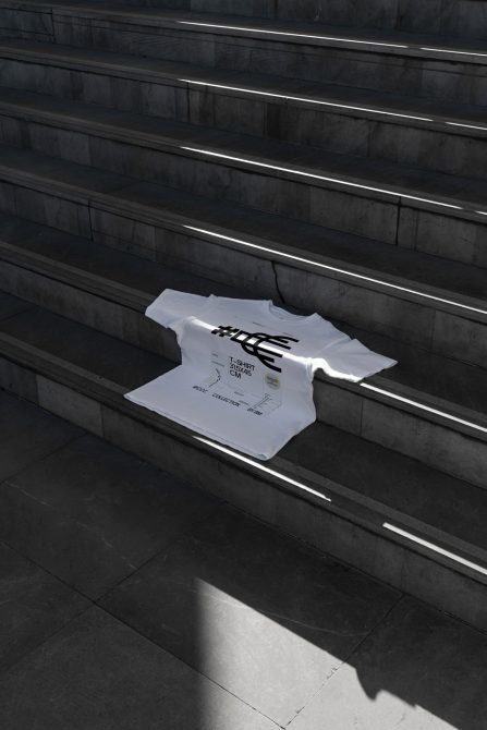 White t-shirt mockup laid flat on dark concrete stairs with graphic print visible