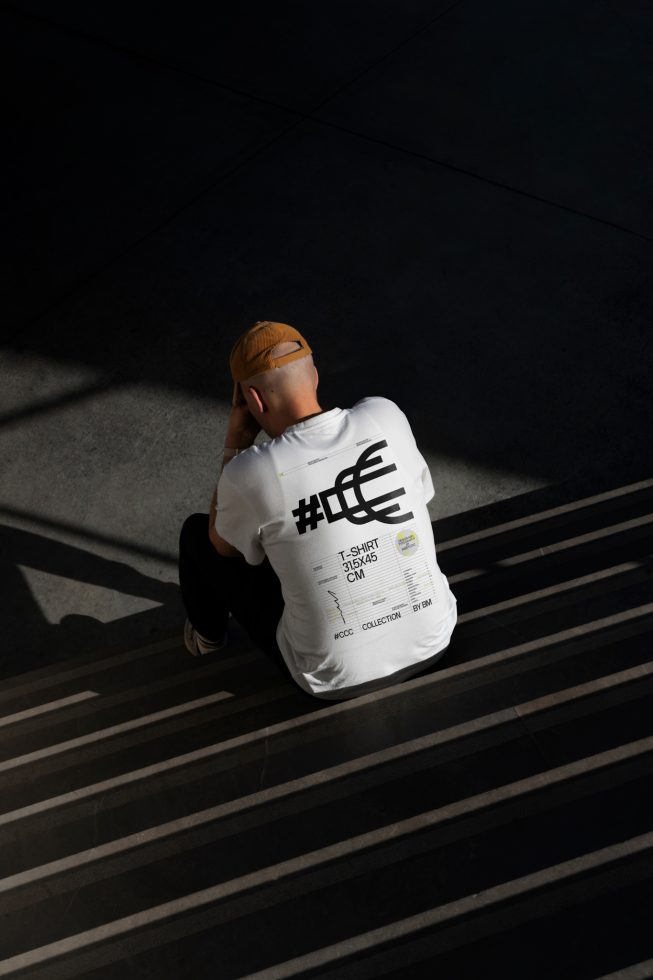 Man in a graphic tee sitting in sunlight with shadows, ideal for t-shirt mockup, urban clothing design template, trendy fashion presentation.