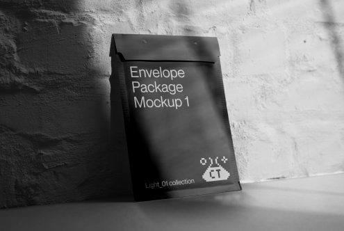 Dark charcoal envelope package leaning against textured white brick wall