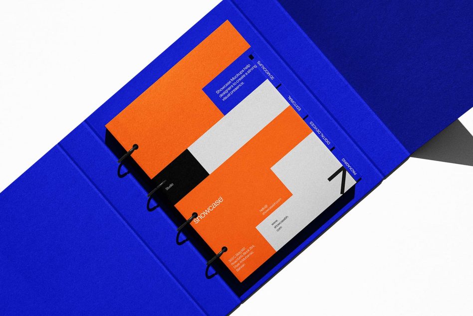 Open portfolio mockup with blue binding and orange graphic design templates laid out for presentation, ideal for showcasing design work.