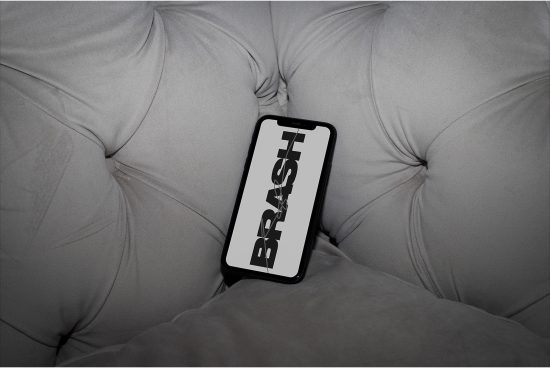 Smartphone mockup with bold font on screen placed on a cushioned sofa for design presentation, ideal for graphics and templates showcase.